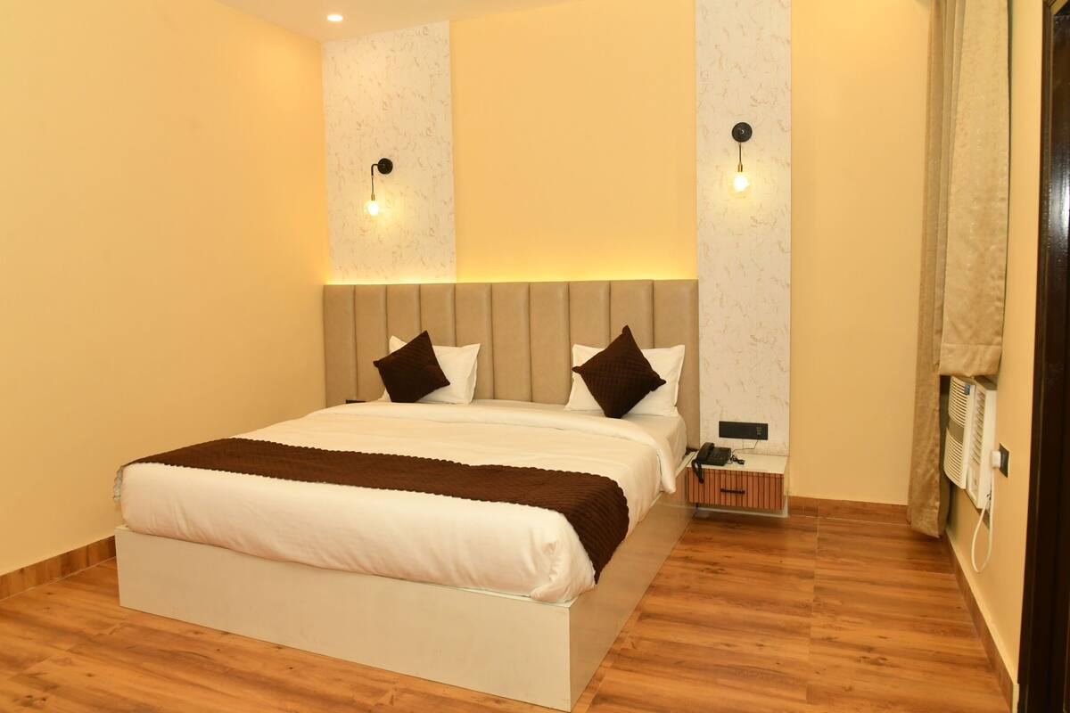 A modern hotel room with a large bed, two wall-mounted lights, a bedside table with a phone, and a wooden floor.