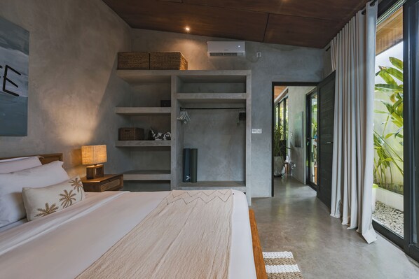 A modern hotel room with a large bed, a walk-in closet, and a view of the outdoors.