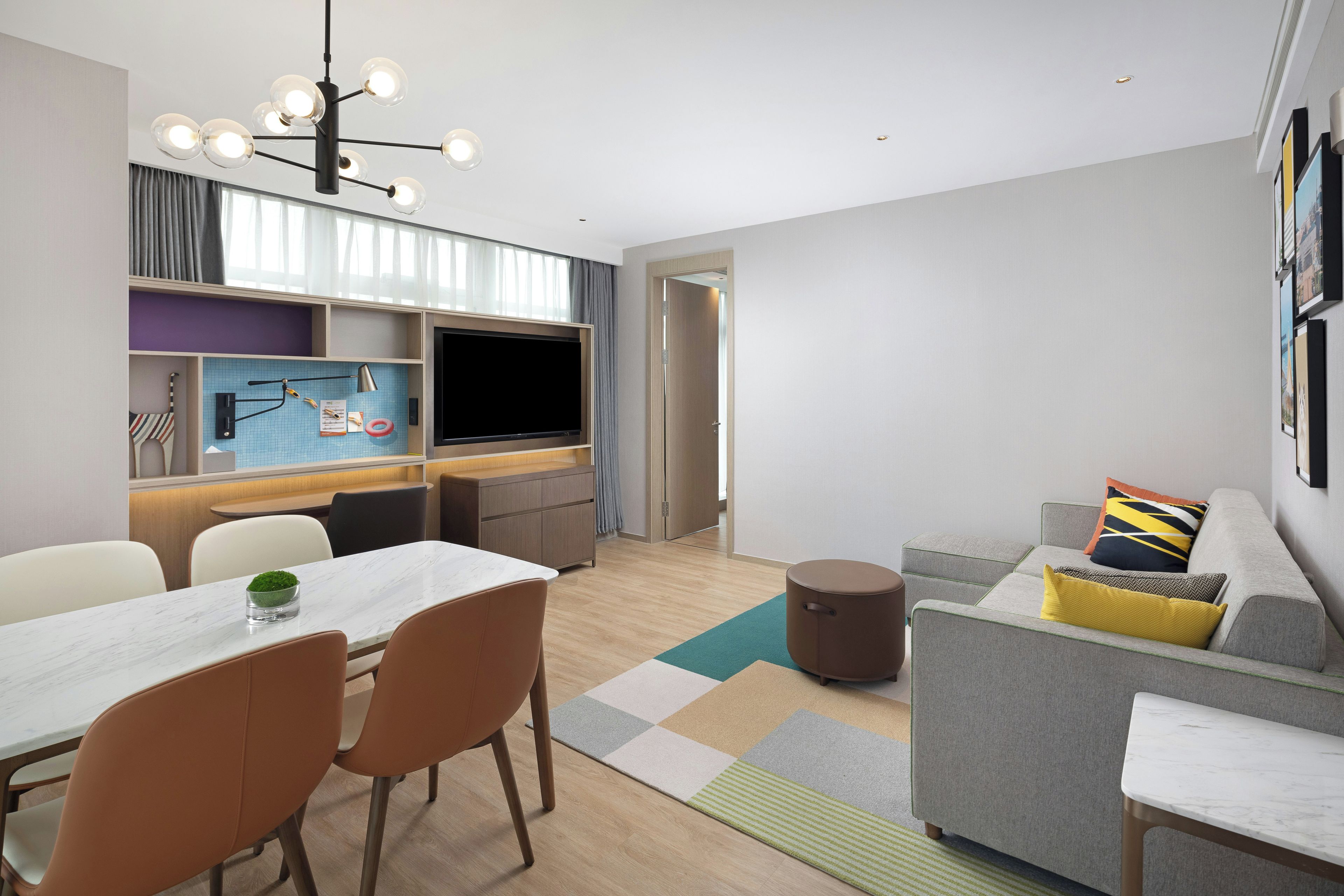 A modern living room with a sofa, a dining table with chairs, a TV, and a kitchen area with a dining table and chairs.