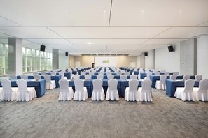 A conference room with rows of tables and chairs, a projector screen, and a large window.