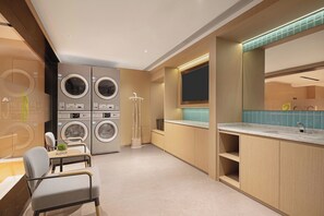 A modern laundry room with stacked washers and dryers, a drying rack, and a sink area with a mirror and countertop.