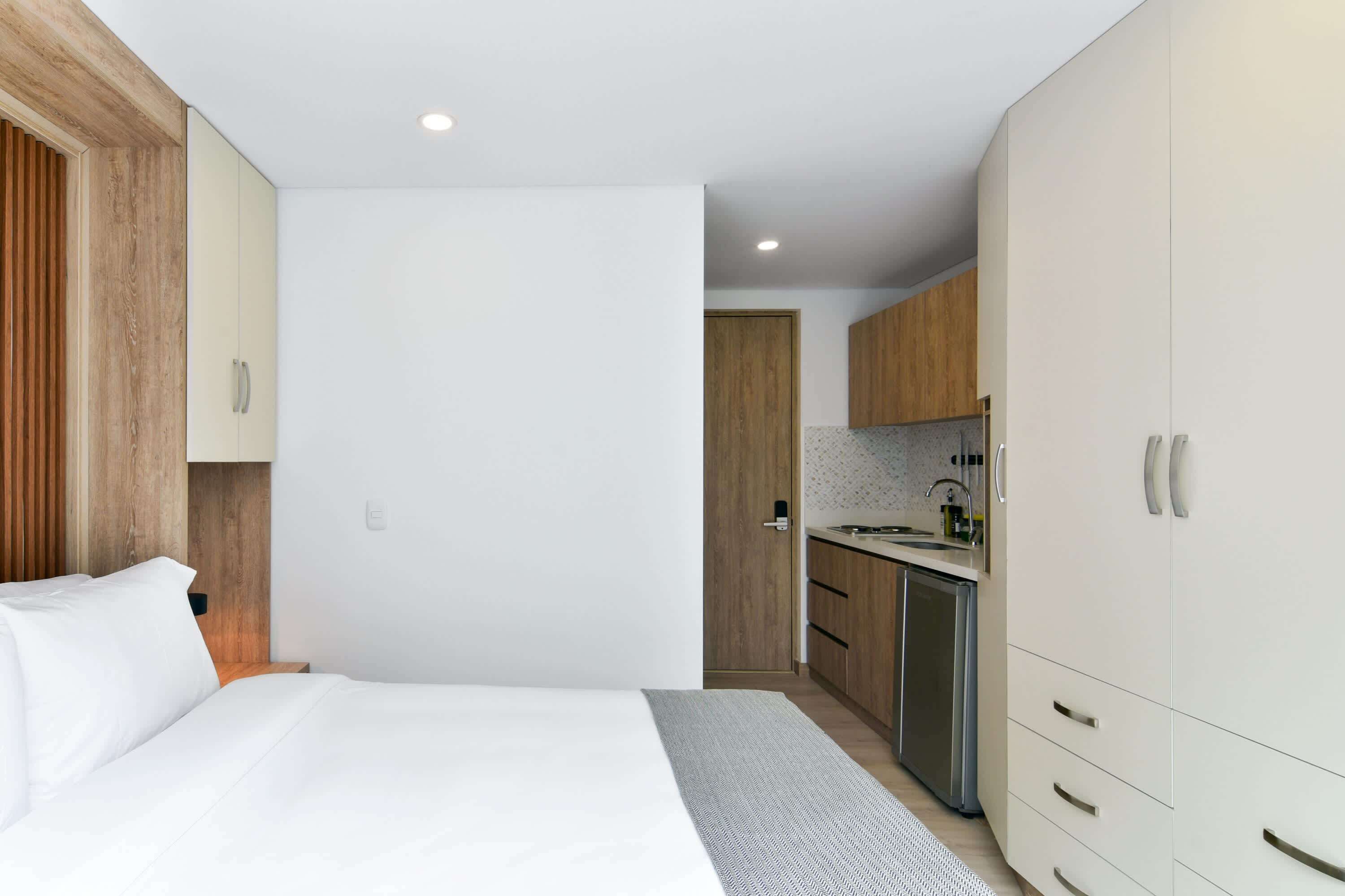 A modern hotel room with a large bed, a small kitchenette, and wooden cabinetry.