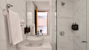 Un baño moderno con lavamanos blanco, un espejo grande, un perchero y una zona de ducha.