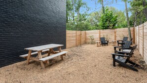 A backyard with a picnic table and chairs, a wooden fence, and trees in the background.