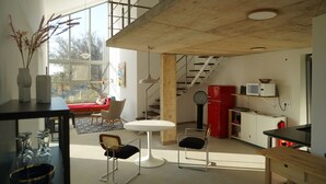 Un espace de vie moderne doté d’un haut plafond, d’un escalier, d’un coin repas avec une table ronde et d’une cuisine avec un réfrigérateur rouge.