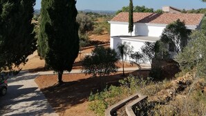 Un bâtiment blanc avec un toit recouvert de tuiles, entouré d’arbres et surplombé d’un ciel bleu clair.