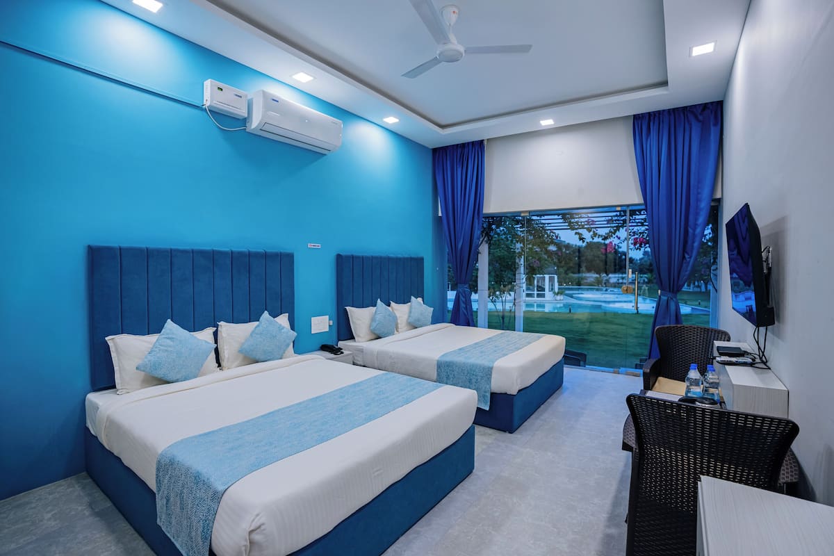 A hotel room with two beds, a desk, a chair, a TV, and a window with curtains.