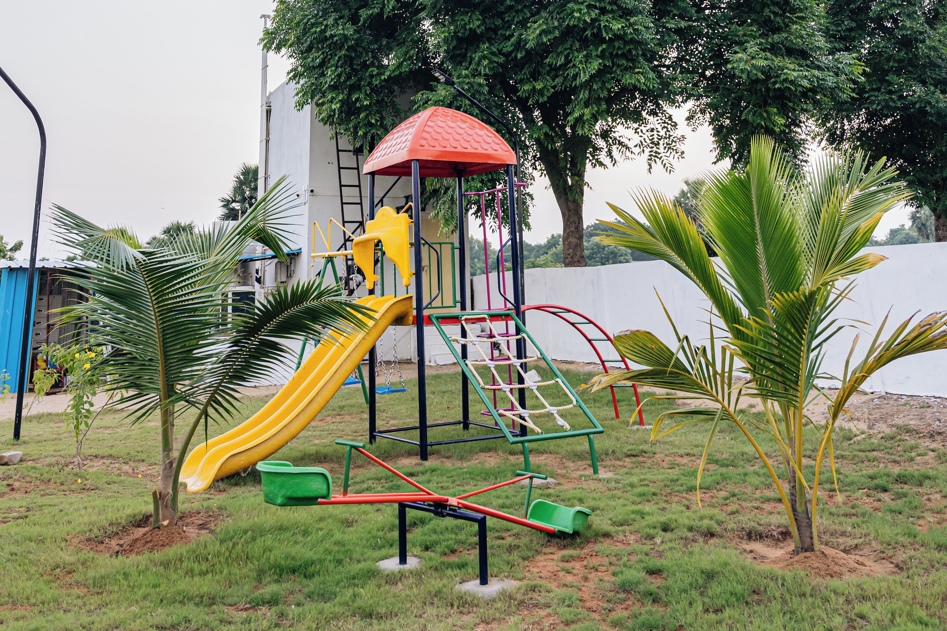 Un parque infantil con un tobogán amarillo, estructuras para escalar y una casita de juegos con techo rojo.