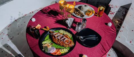 A round table with a red tablecloth, a plate of food, a glass of drink, and candles.