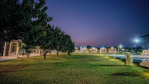 Uma área externa bem iluminada com gramado, árvores e uma fileira de edifícios modernos com telhados azuis.