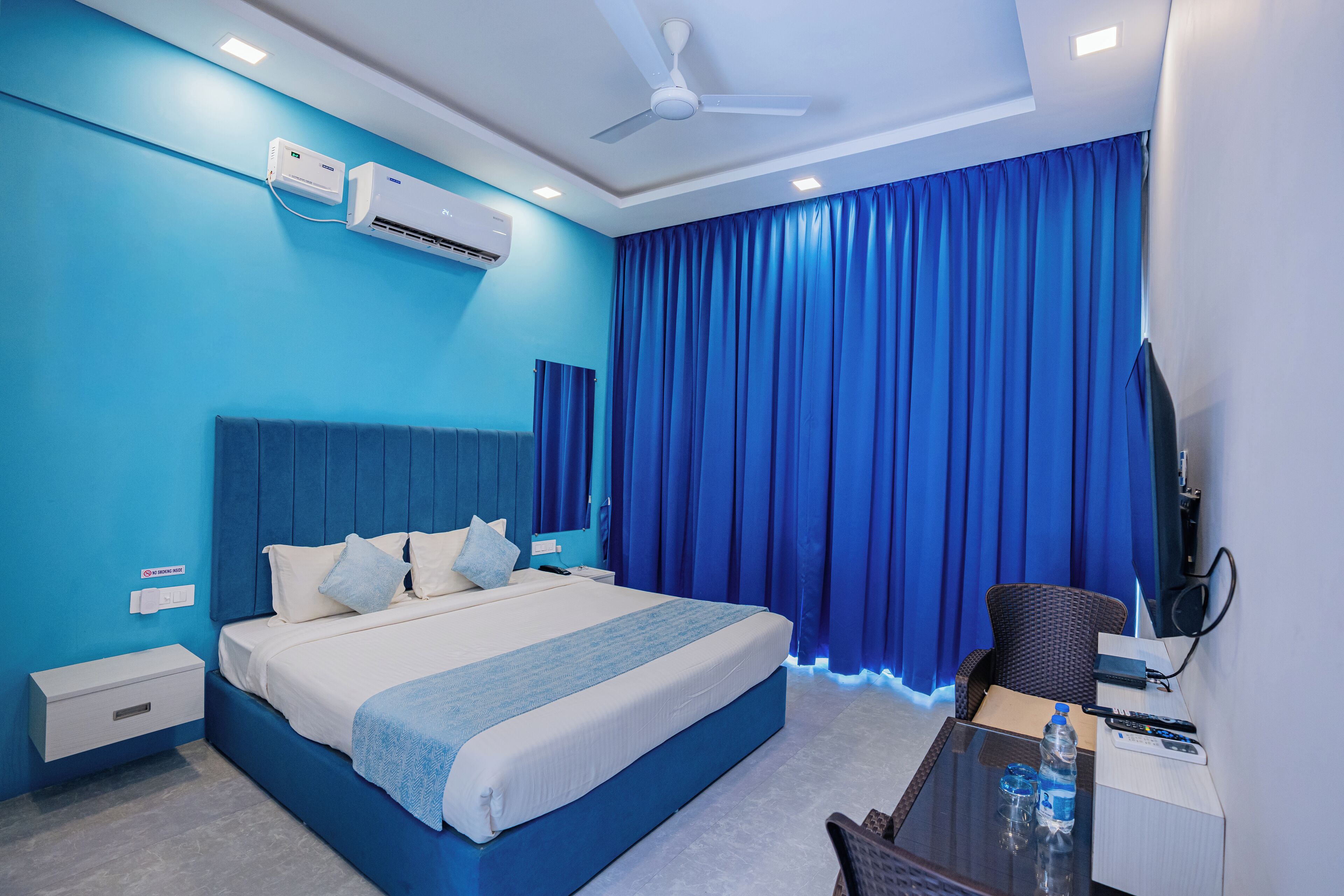 A hotel room with a bed, a desk, a chair, a television, and an air conditioning unit.
