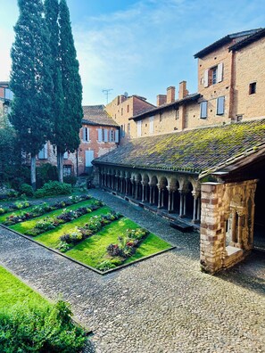 A courtyard with a garden, stone pathway, and traditional buildings with brick facades and tiled roofs.