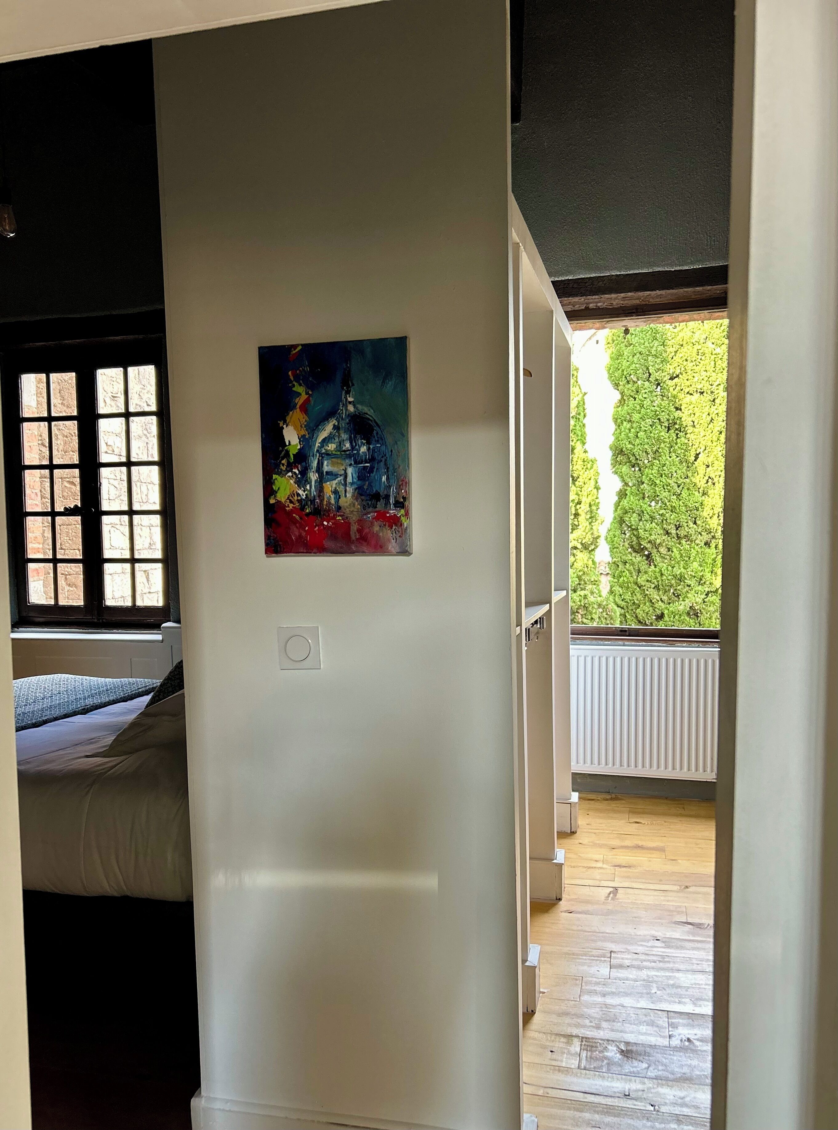 Een kamer met een bed, een raam met uitzicht op groen en een schilderij aan de muur.