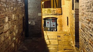 A narrow, dimly lit corridor with brick walls and a wooden ceiling. A small, barred window with a sign is visible in the distance. - La Maison du Prévôt, au Pied de la Cathédrale ! (Albi)
