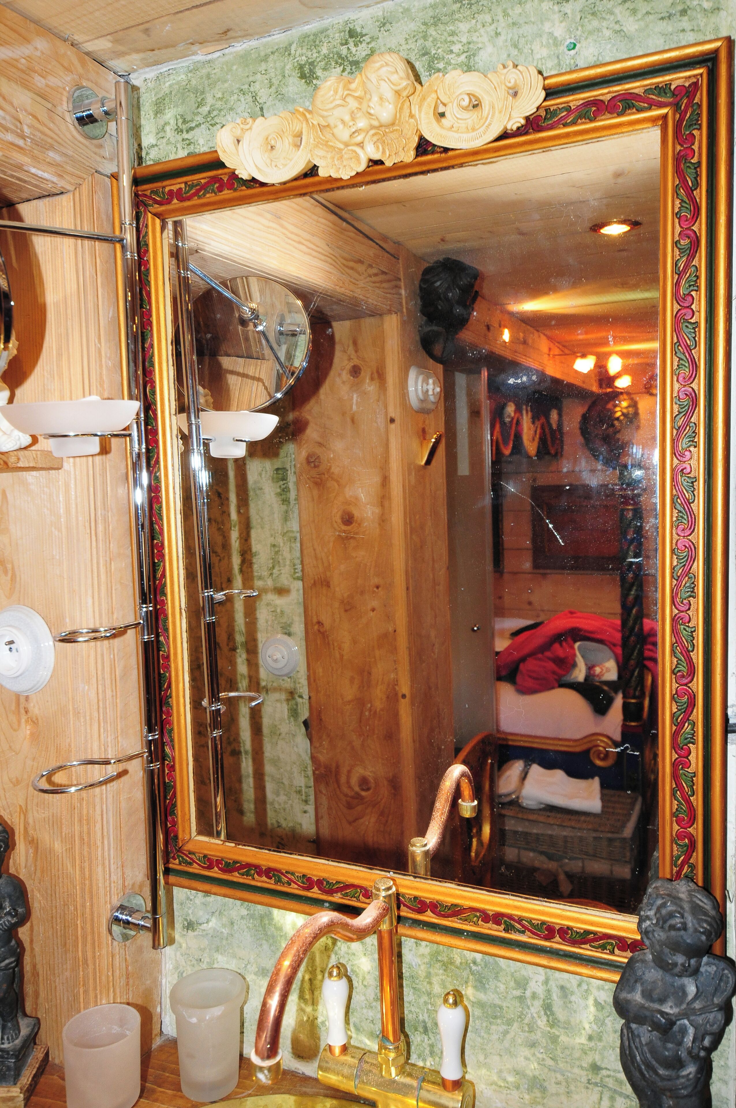 A bathroom with a large ornate mirror, wooden walls, and a vintage-style sink with a copper faucet.