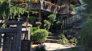 A multi-level wooden structure with balconies, surrounded by lush greenery and flowering plants. - Hôtel Les Chalets de Philippe avec Jacuzzis privatifs (Chamonix-Mont-Blanc)