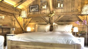 A wooden cabin bedroom with a large bed, wooden walls, and a sloped ceiling. - Hôtel Les Chalets de Philippe avec Jacuzzis privatifs (Chamonix-Mont-Blanc)