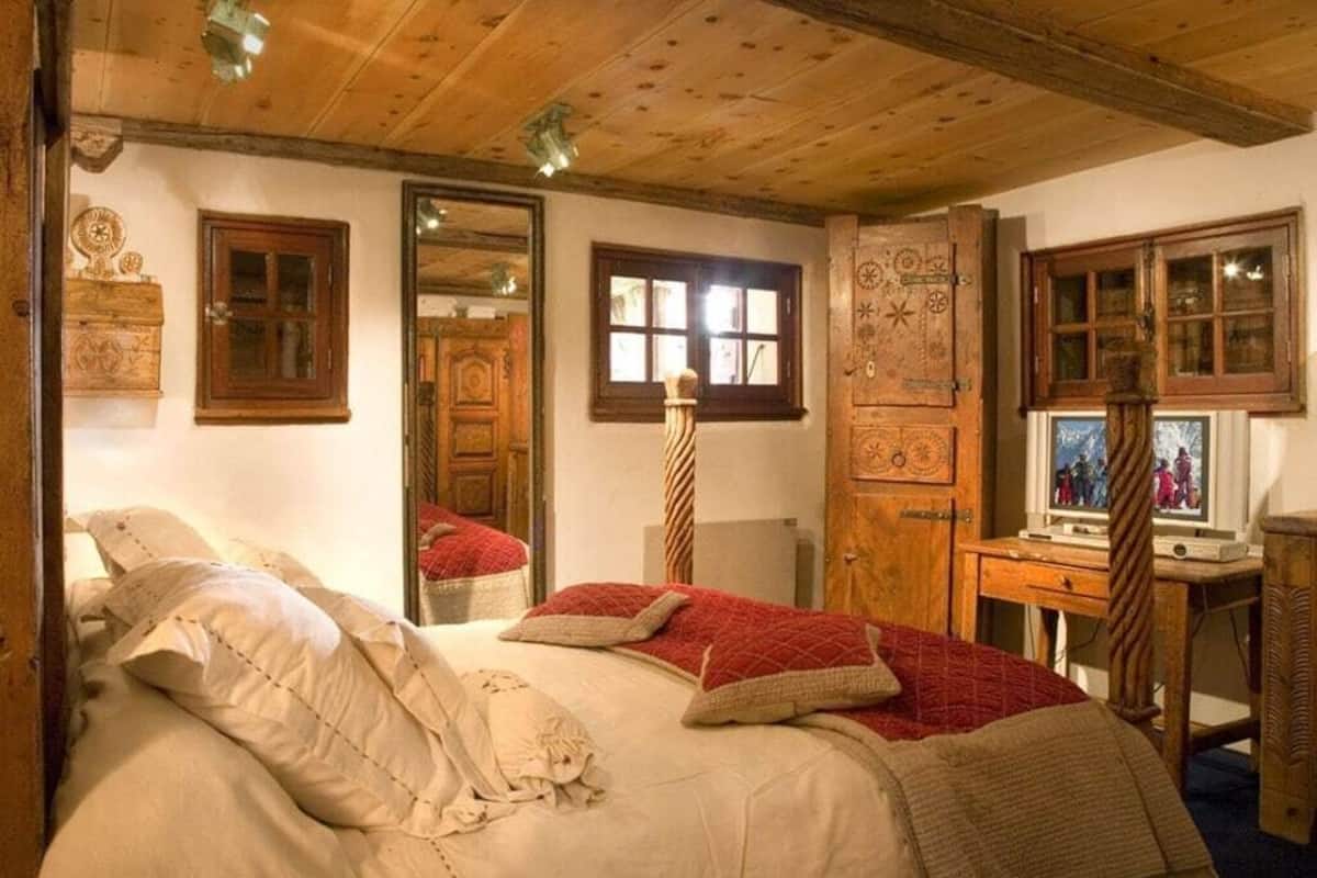 Una camera tradizionale con soffitto in legno, un letto con biancheria rossa e bianca, una scrivania in legno con un computer e uno specchio appeso al muro.