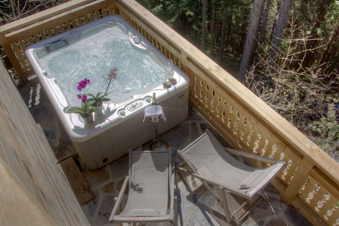 A hot tub on a wooden deck with two chairs and a bottle of champagne.