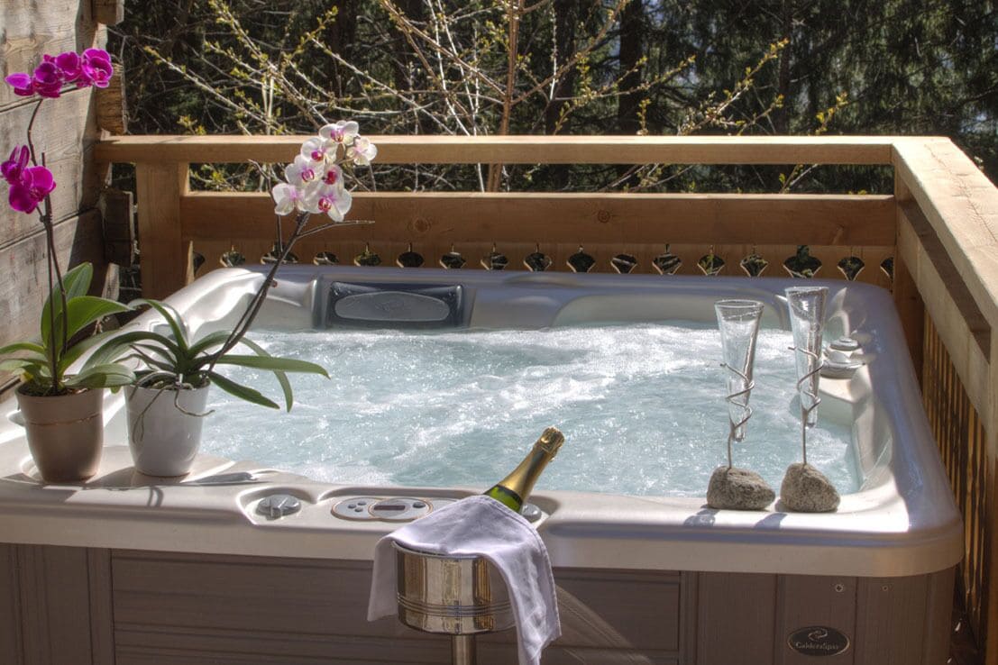 Un jacuzzi con terraza de madera, dos plantas en macetas, una botella de champán y dos copas.