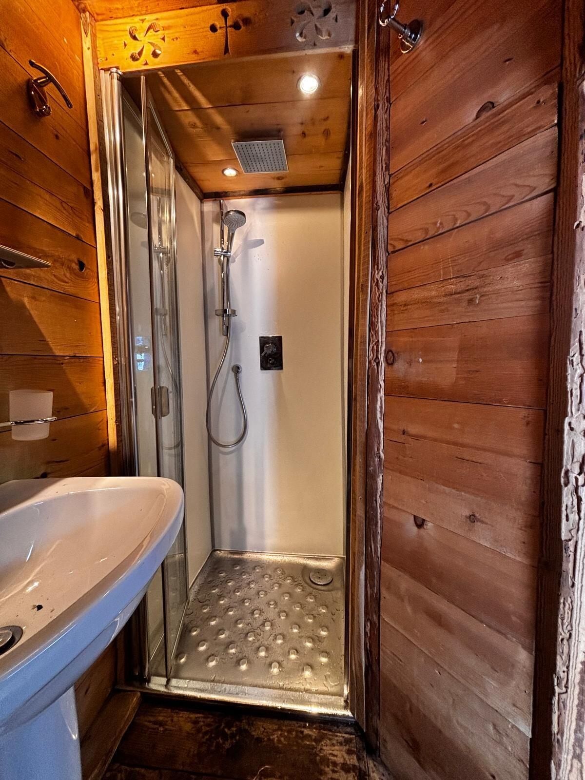 A wooden cabin interior with a shower area, a sink, and a ceiling vent.
