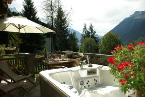 Un balcon avec un jacuzzi, des chaises en bois, une table dressée pour le repas et un grand parasol.