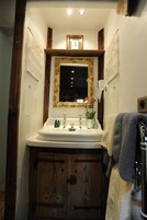 A bathroom with a wooden vanity, a white sink, a mirror with a gold frame, and a small framed picture above the mirror.