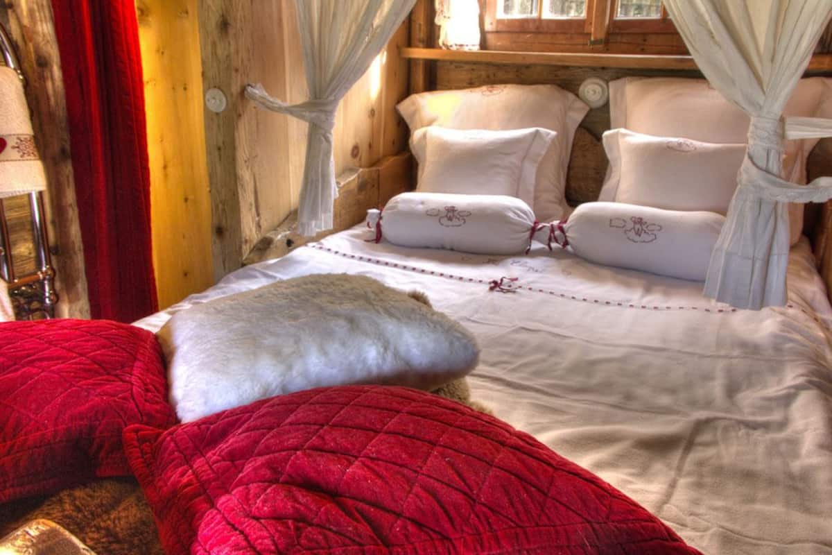 Camera da letto in una baita di legno, con un letto e biancheria rossa e bianca, e una tenda.