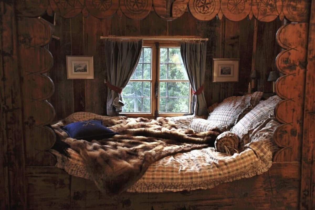 Una stanza rustica in legno con un letto, due quadri appesi e una finestra con tende.