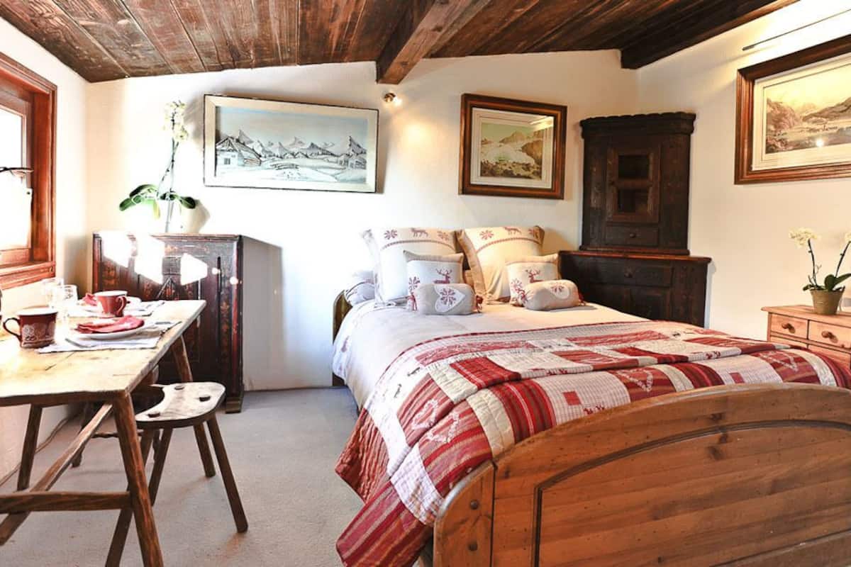 Una camera accogliente con un letto di legno, una scrivania con una sedia e un comò. Alle pareti ci sono quadri incorniciati e una finestra con tende.
