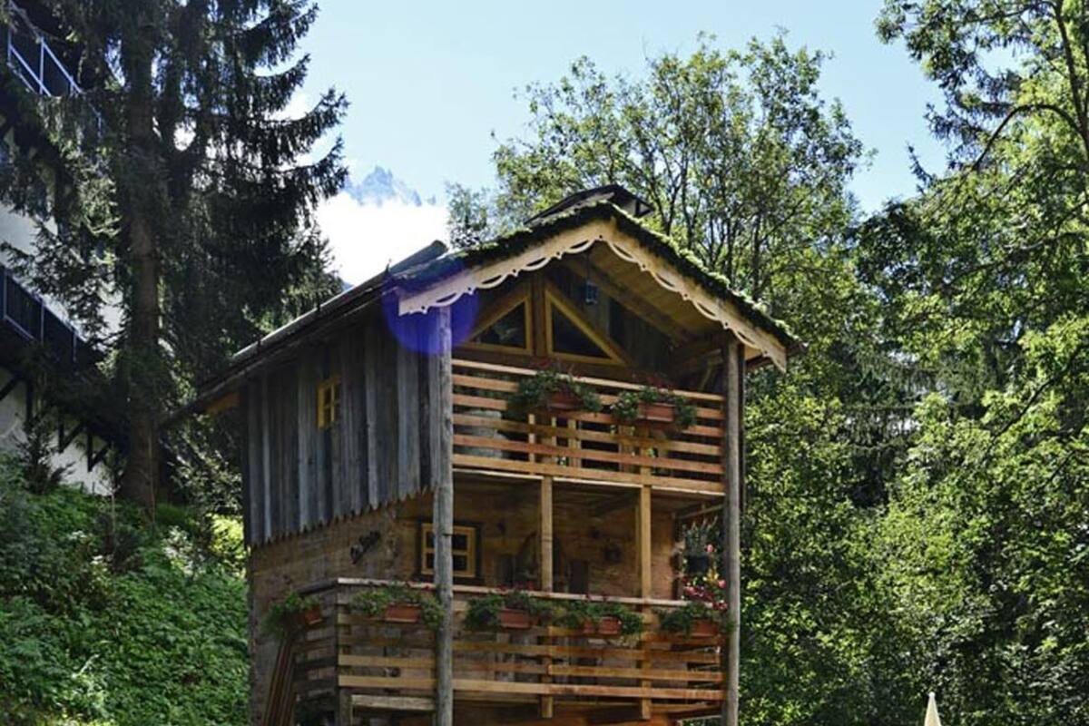 Una baita di legno con diversi balconi, immersa nel verde e con un vialetto in pietra.