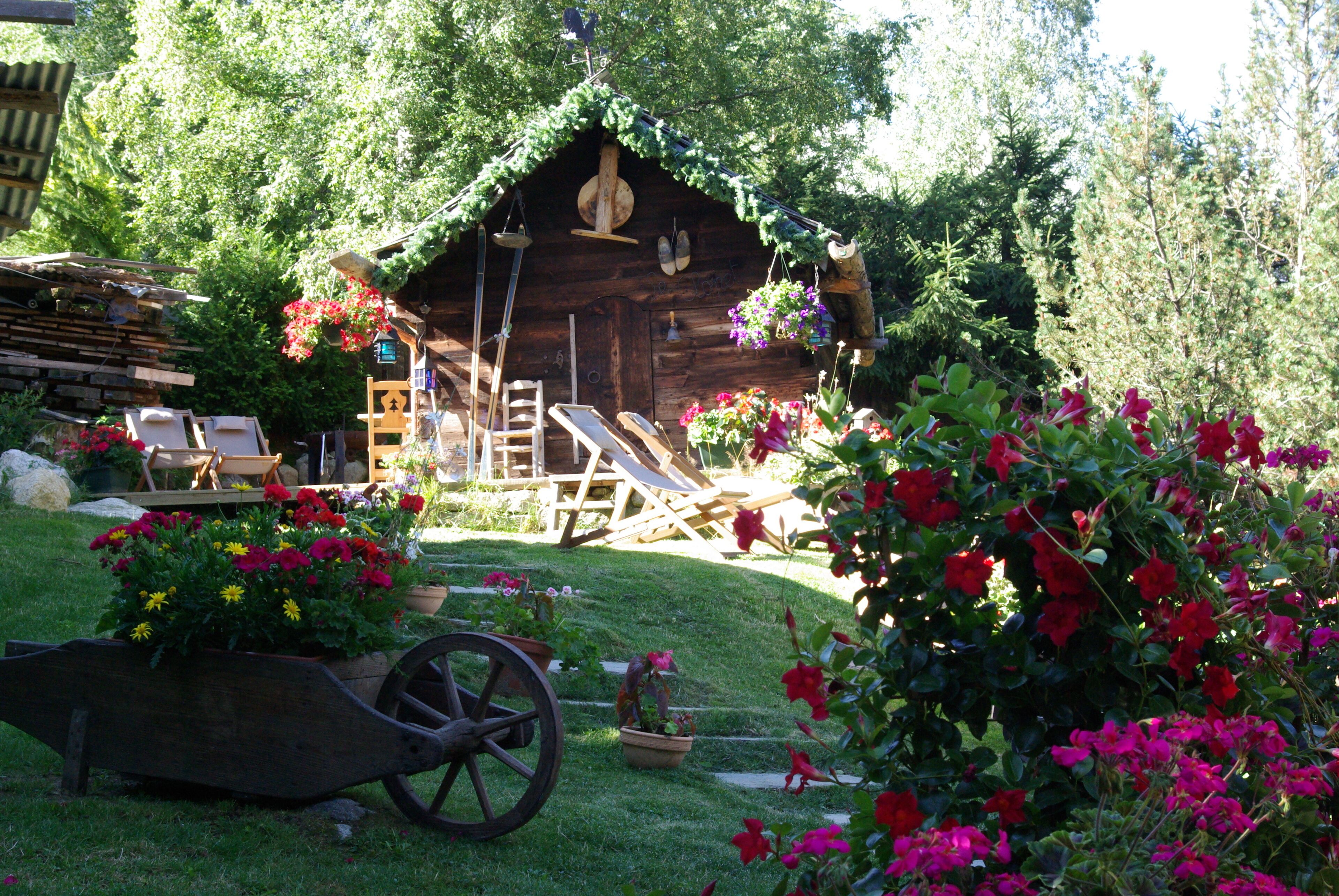 A rustic wooden cabin with a thatched roof, surrounded by lush greenery and vibrant flowers.