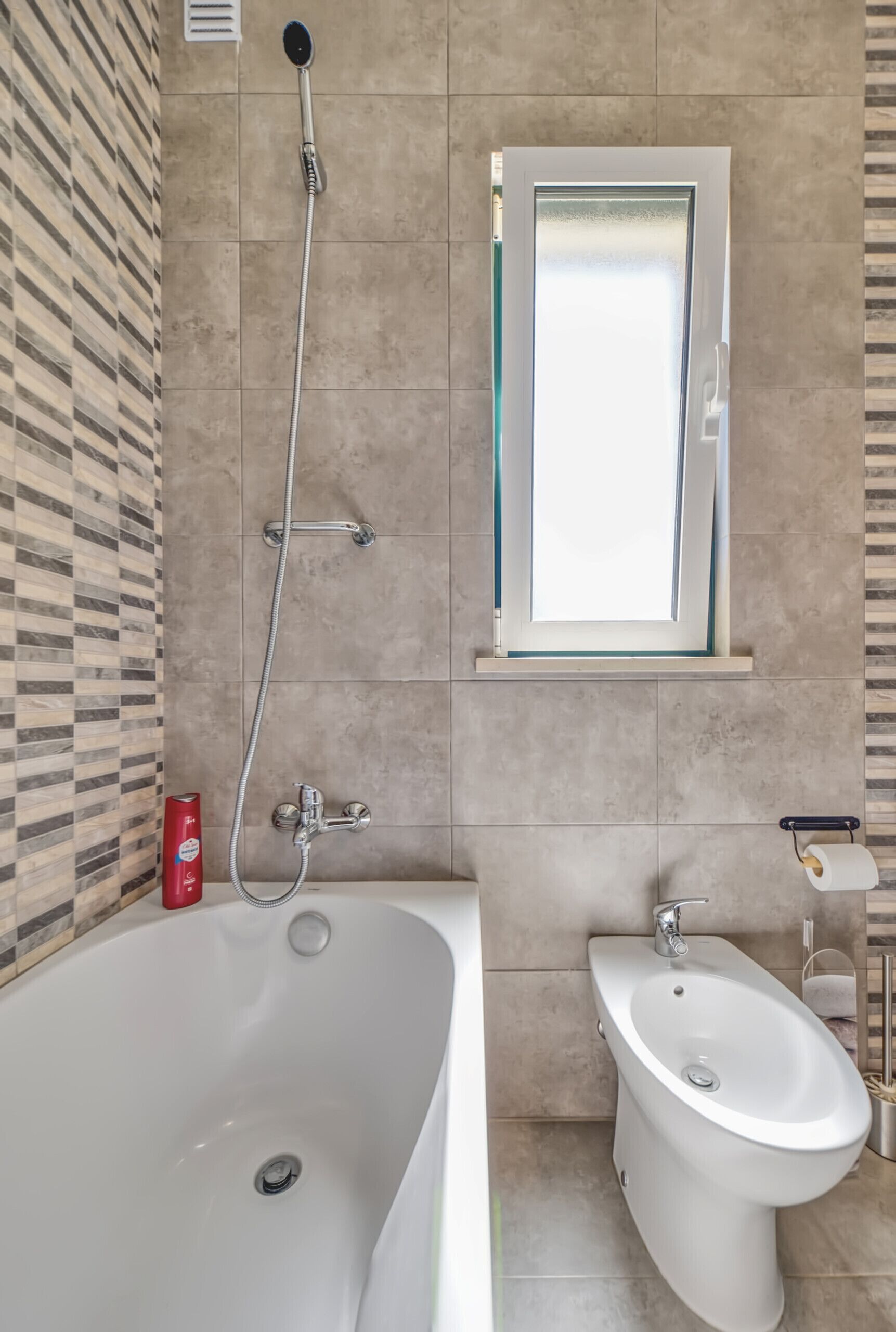 A modern bathroom with a bathtub, a bidet, and a window above the sink.