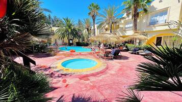 Un área de piscina con varias piscinas, sillas de descanso y palmeras.