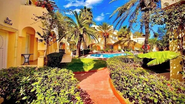 A resort with a swimming pool, palm trees, and a pathway leading to the pool area. - Appart'hotel de charme  (Hammamet)