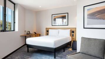 Habitación de hotel con cama, mesita de noche, silla y obras de arte en las paredes.