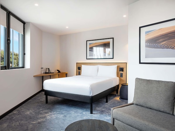 Habitación de hotel con cama, mesita de noche, silla y obras de arte en las paredes.