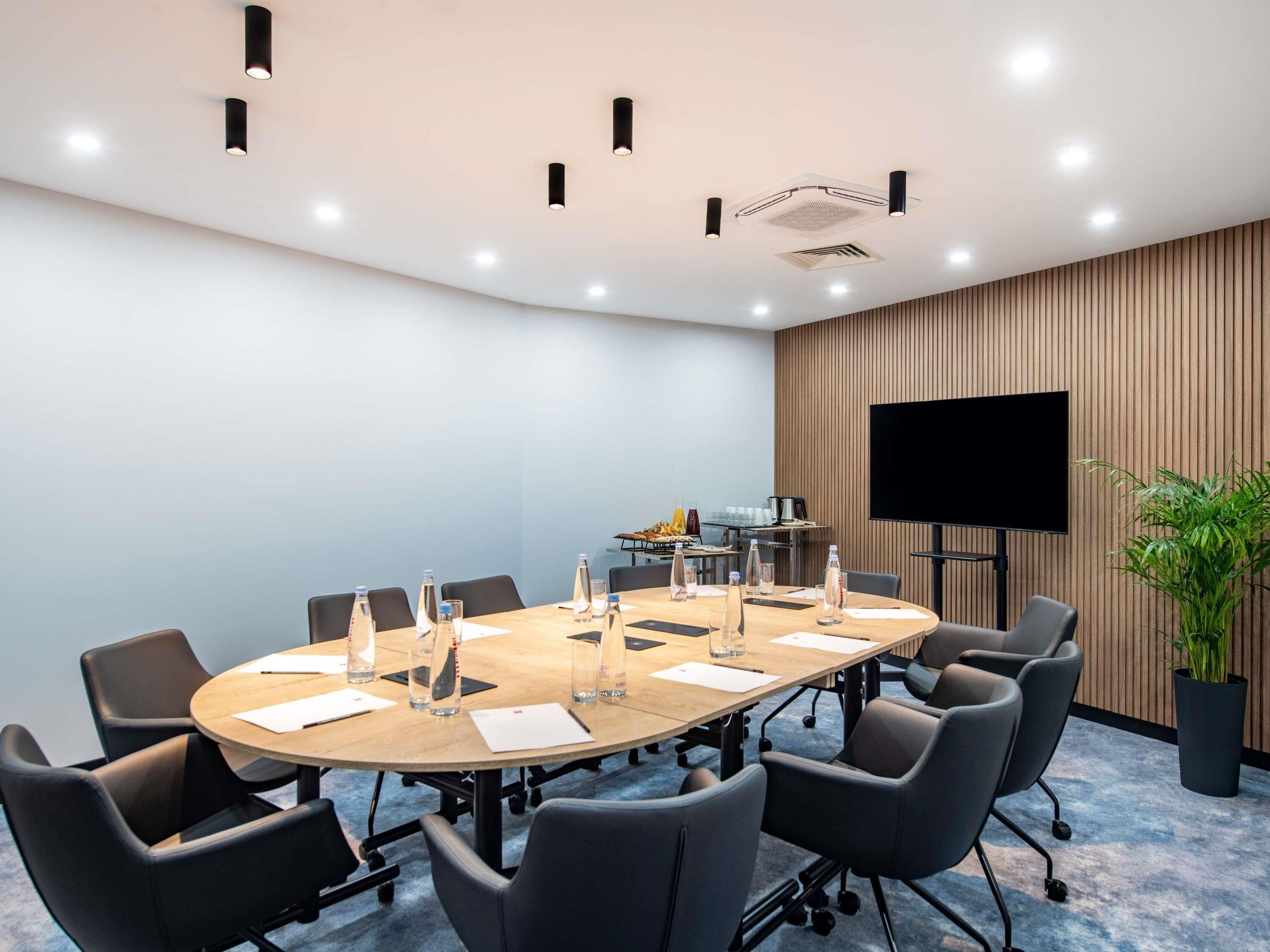 A conference room with a large table, chairs, a flat-screen TV, and a plant.