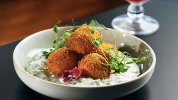 A plate of breaded balls with a creamy sauce and garnishes, accompanied by a glass of red drink.