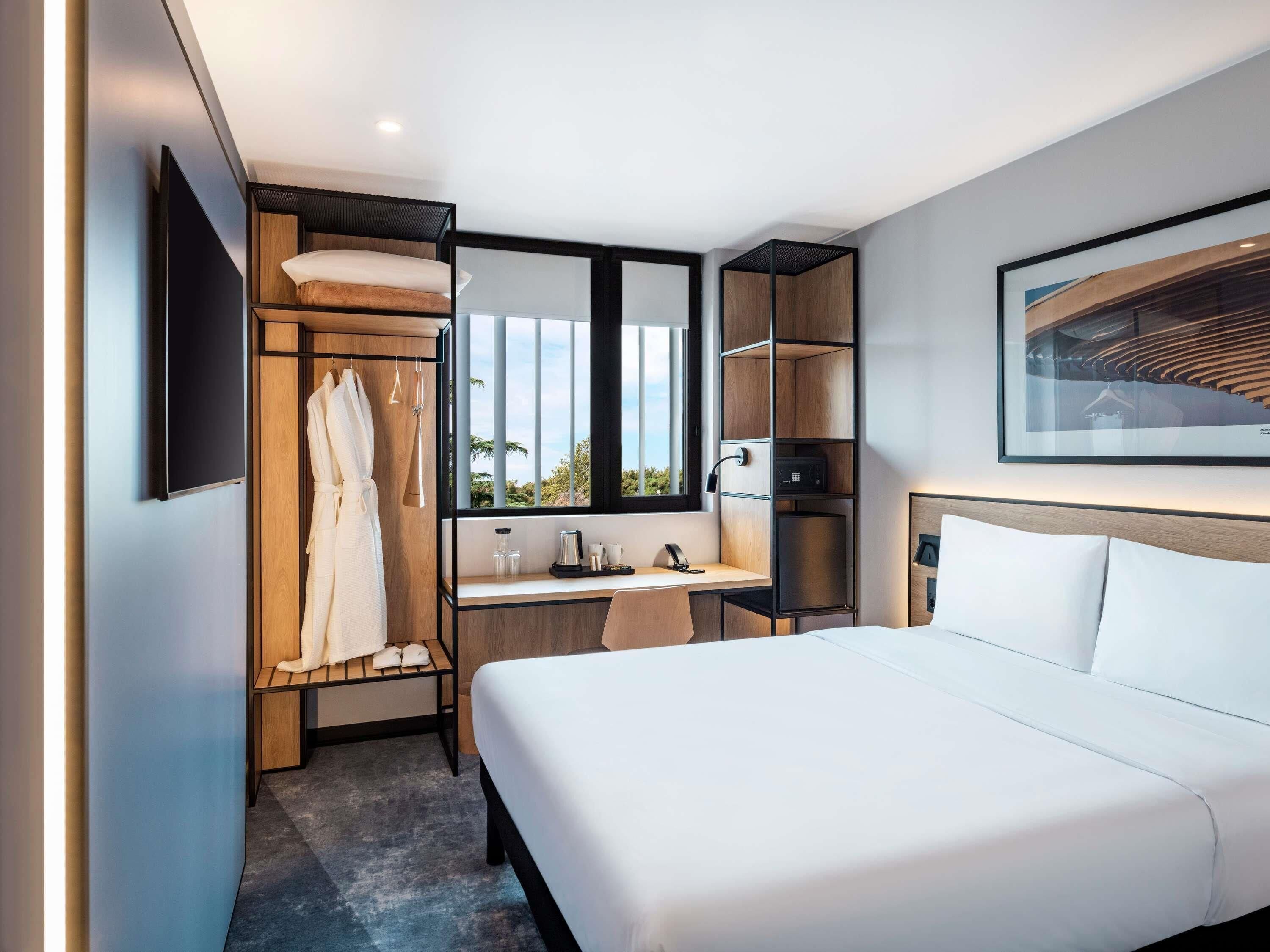 Ein Hotelzimmer mit Bett, Schreibtisch, Kleiderschrank und einem großen Fenster.