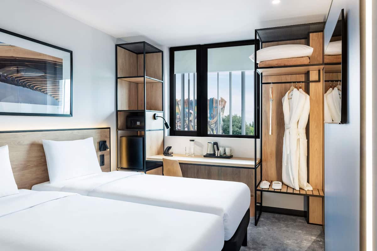 Ein modernes Hotelzimmer mit zwei Betten, einem Schreibtisch, einem Kleiderschrank und einem großen Fenster.
