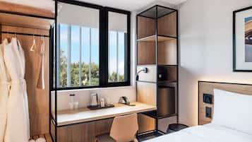 Quarto de hotel moderno com cama, escrivaninha, cadeira, guarda-roupa e uma janela grande.