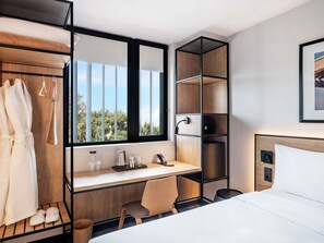 A modern hotel room with a bed, a desk, a chair, a wardrobe, and a large window.