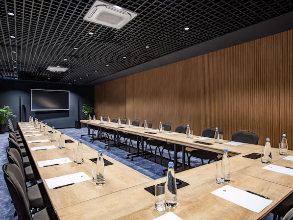 Ein Konferenzraum mit langem Tisch, Stühlen, Wasserflaschen und einer Projektionsleinwand.