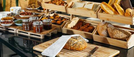 A buffet with various breads, pastries, and condiments.