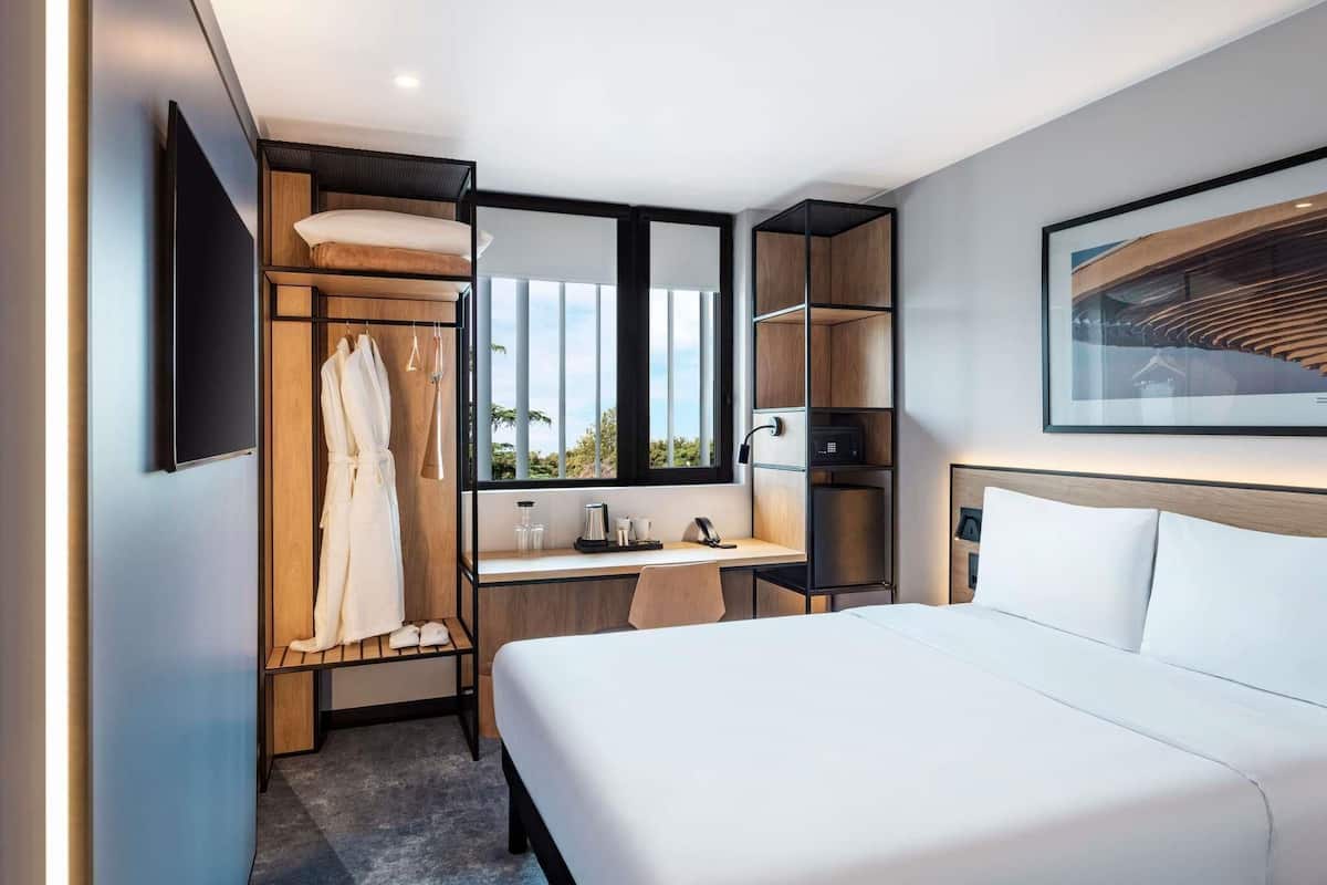 Ein modernes Hotelzimmer mit Bett, Schreibtisch, Kleiderschrank und großem Fenster.
