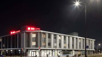 A modern hotel with a prominent 'ibis HOTEL' sign, large windows, and a well-lit facade.
