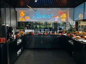 Interior de una cafetería con un letrero de neón, máquinas de café y una variedad de alimentos.