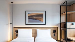 A hotel room with two beds, a framed picture on the wall, and a built-in wooden shelf unit.