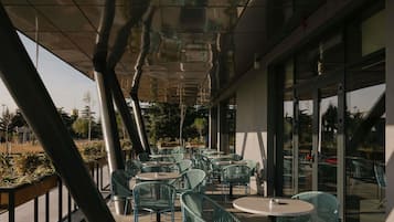 Uma área externa com mesas e cadeiras, janelas amplas e um design arquitetônico moderno.